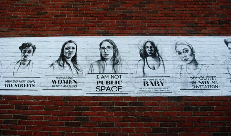 Posters of the "Stop Telling Women to Smile" campaign are displayed on a brick wall