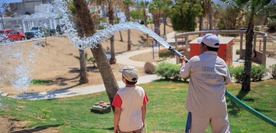 A person is wielding a hose, which is releasing a stream of water, while a youngster is observing.