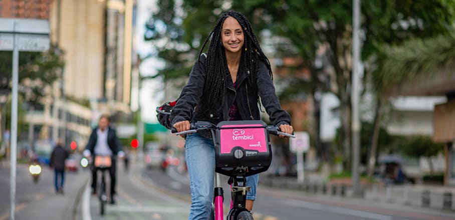 A young woman with dread locks is riding a pink share bike.