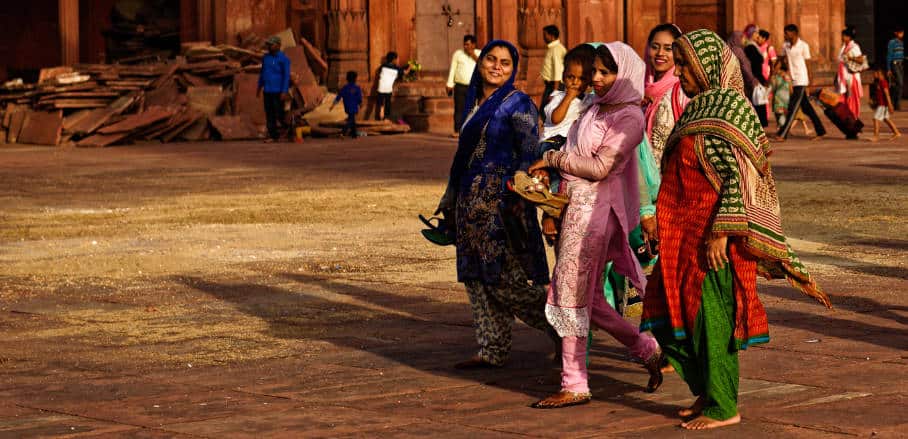 4 women in India, one holding a small child, are walking together smiling.