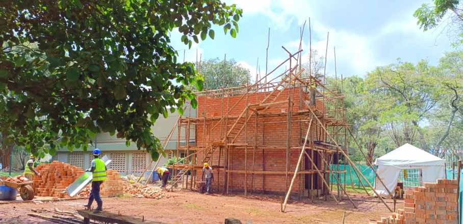 A construction site showing a cube house made of bricks and construction workers in front