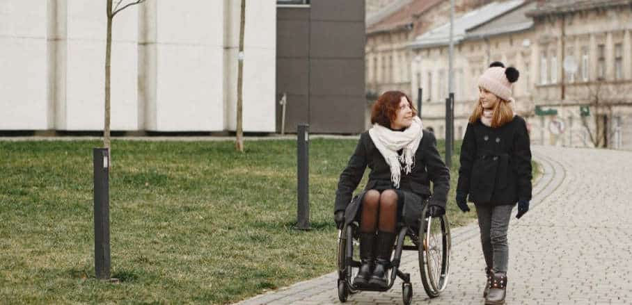 ﻿﻿Disabled woman in wheelchair with daughter, walking outside in the park.