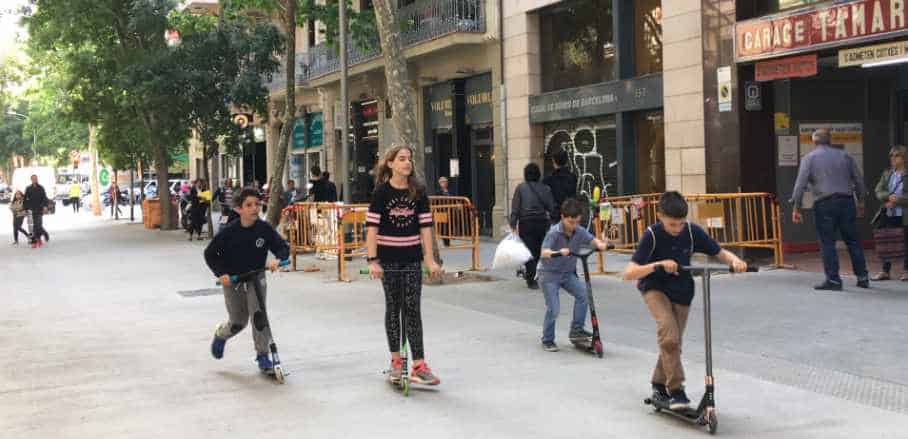 Children are riding their scooters down a street in Barcelona. 