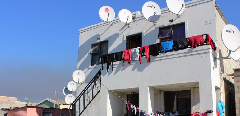 A white house with several satellite dishes and colorful lothes hanging from a clothlines.
